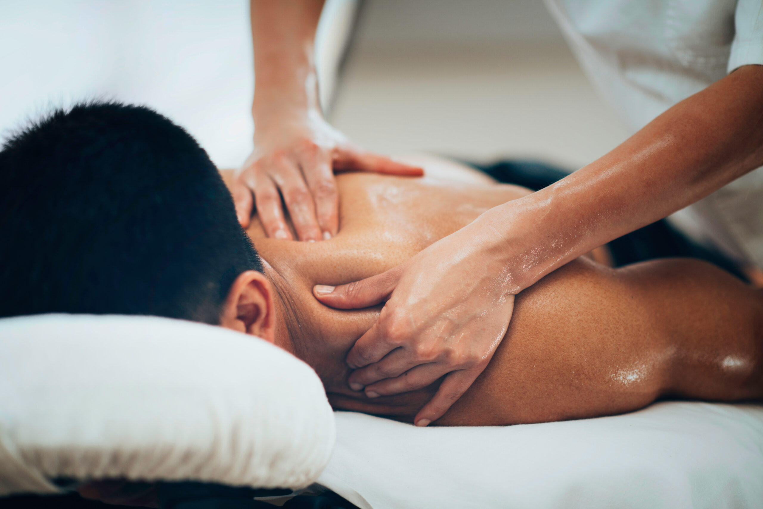 A massage therapist kneads the shoulder and upper back muscles of a male client during a deep tissue massage therapy session.