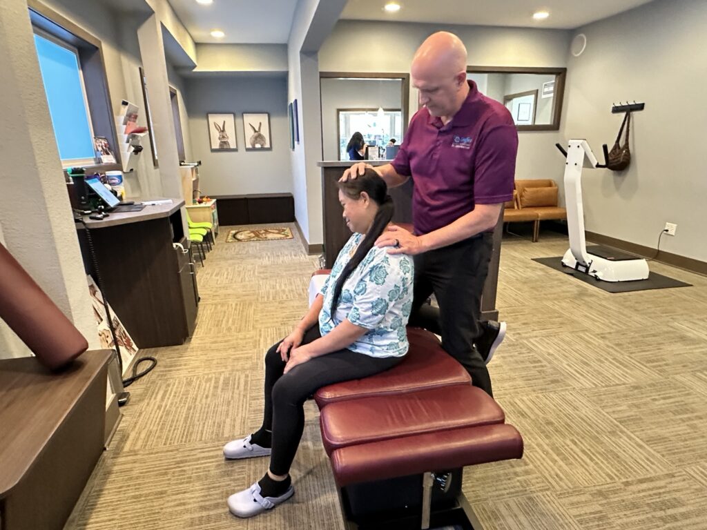 Chiropractor performing a neck examination and adjustment on a seated female patient in a medical clinic setting.